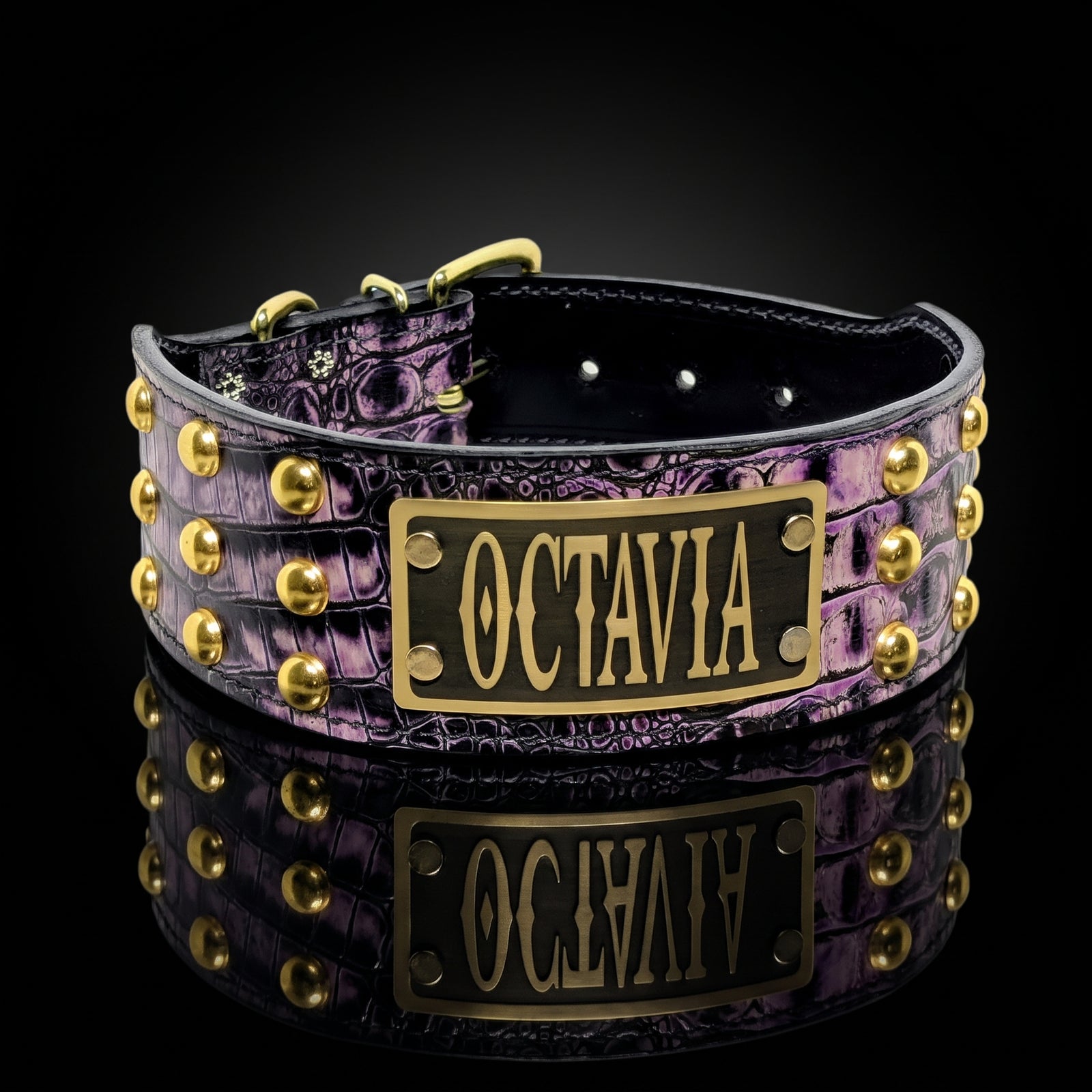 A purple crocodile-embossed leather collar with gold studs and a black plaque engraved with the name 'OCTAVIA' in gold lettering, shown on a reflective black background.