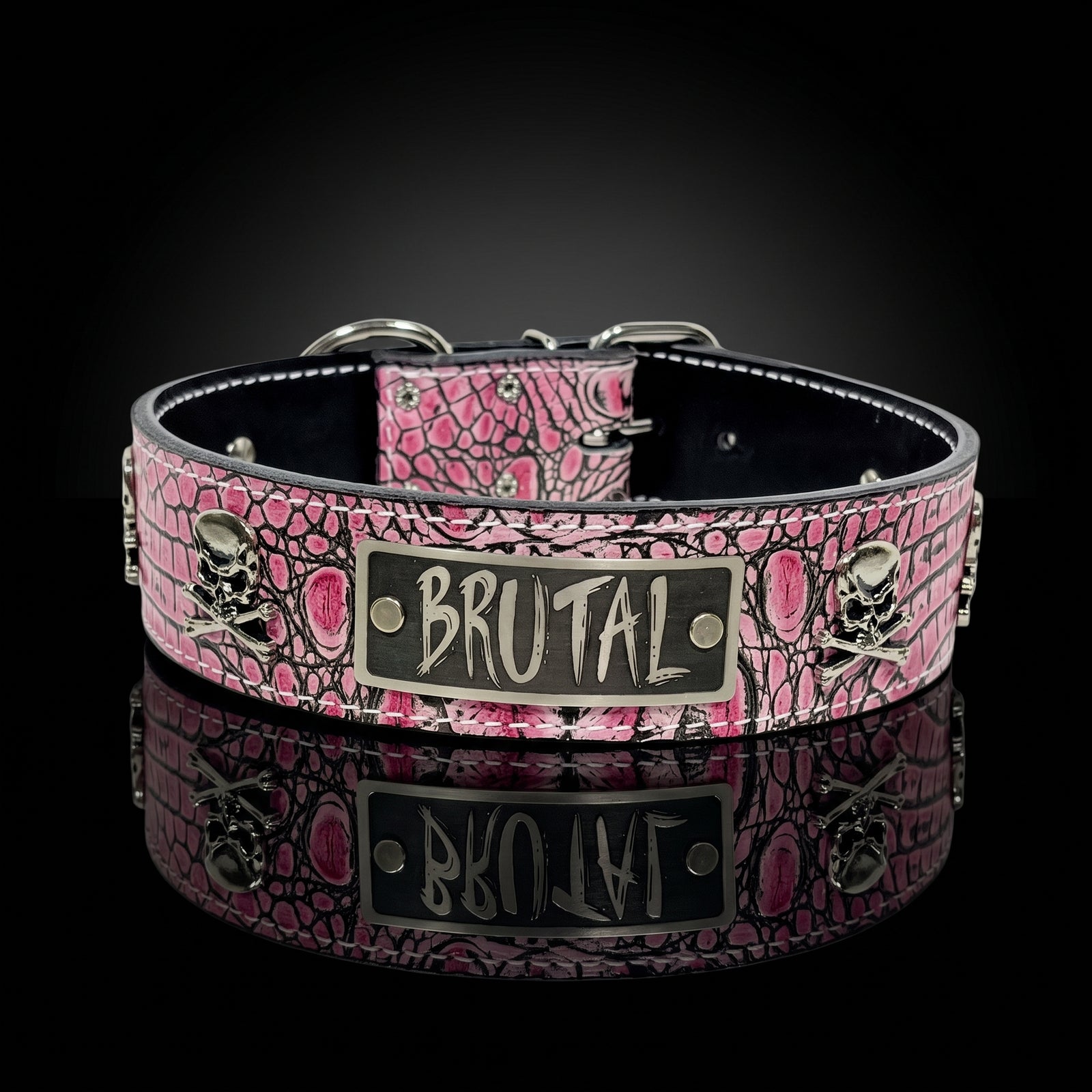 A pink and black snakeskin-patterned collar with silver-tone hardware, featuring a central rectangular plate engraved with the word 'BRUTAL' and skull-and-crossbones motifs on both sides, shown on a black reflective background.