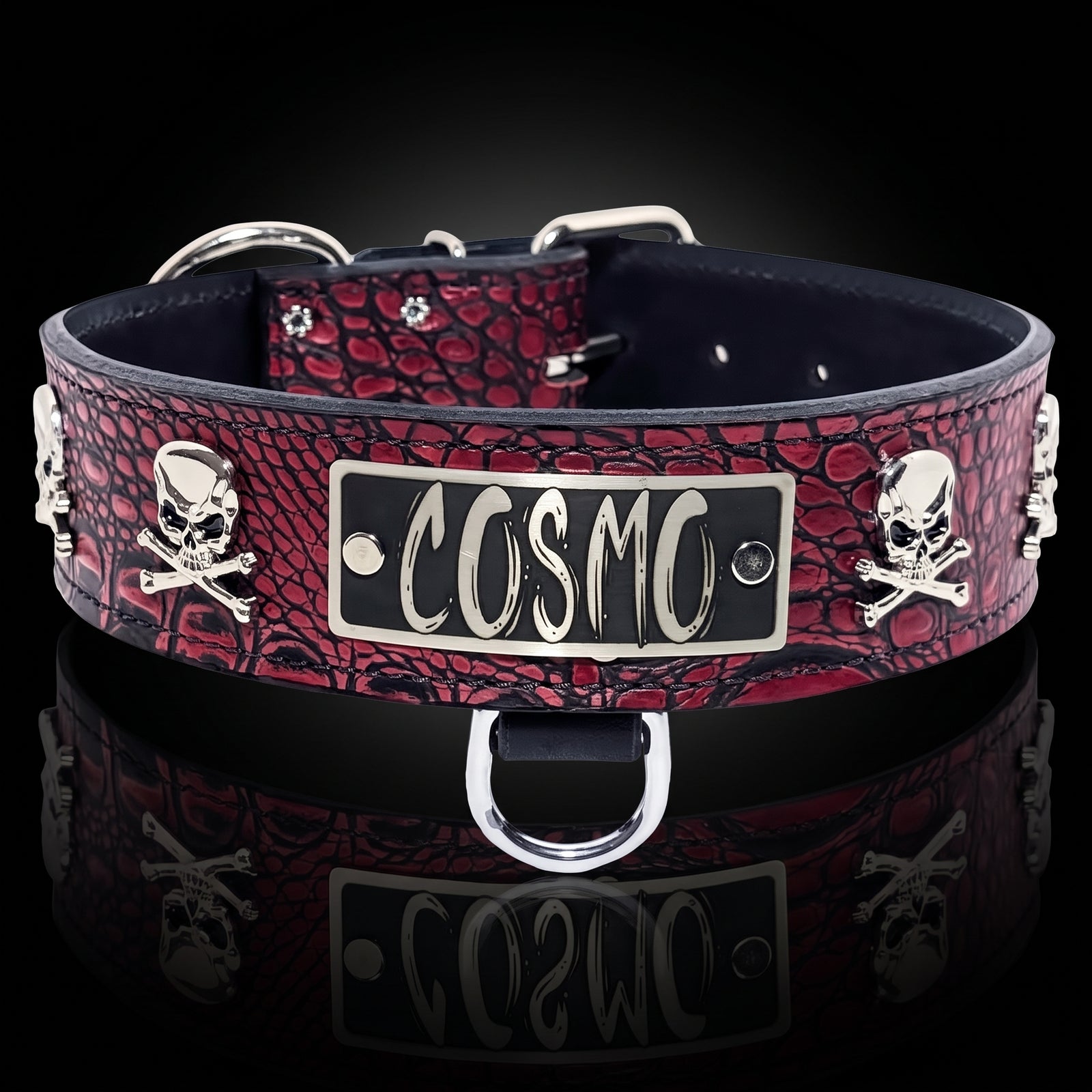A red and black crocodile-embossed leather collar with silver-tone metal hardware, featuring skull and crossbones motifs and a central rectangular plate engraved with the word 'COSMO'.