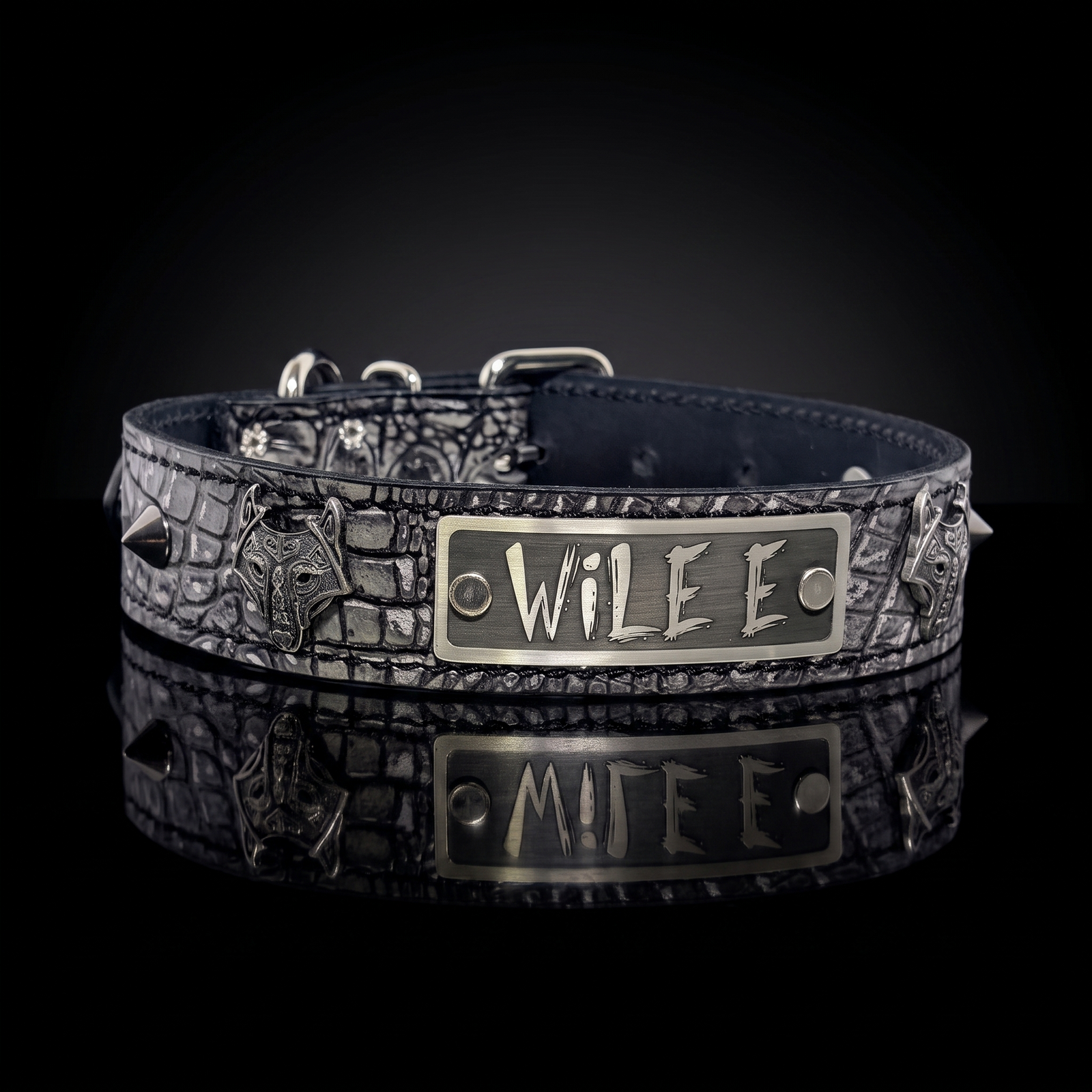A dark textured dog collar with a central silver-tone metal plate engraved with 'WILE E', displayed on a reflective black surface against a black background.