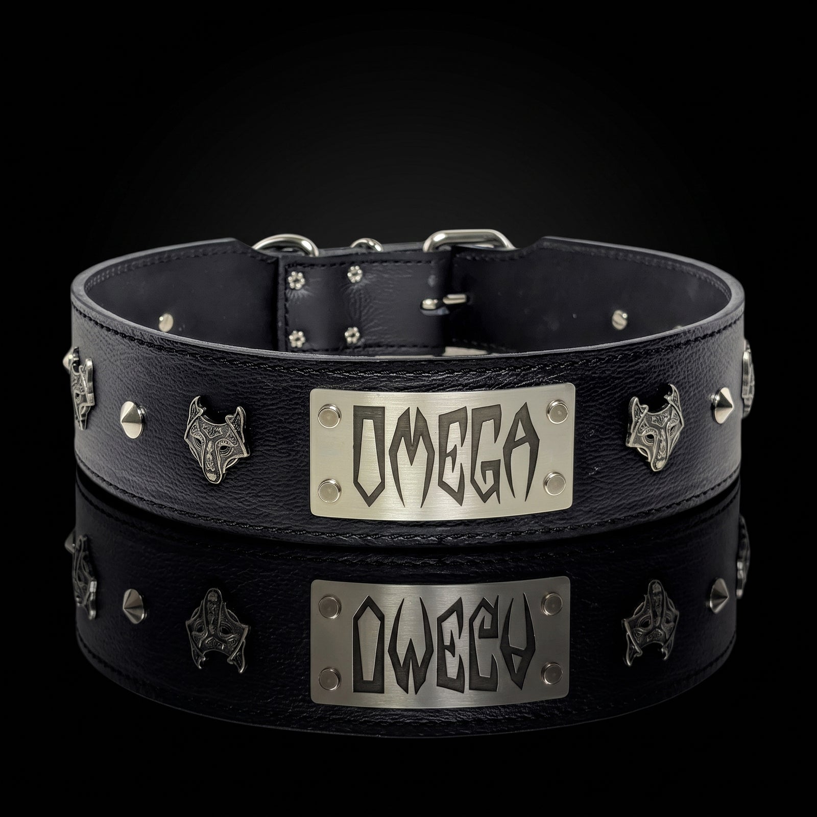 A black leather collar with silver metal studs, wolf head emblems, and a central rectangular silver plate engraved with the word 'OMEGA', shown on a black background with a reflection below.