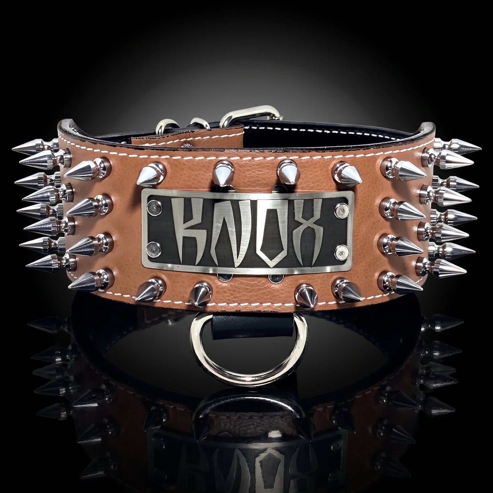 A tan leather spiked collar with a central silver metal plate featuring the stylized text 'KNOW'. The collar is adorned with multiple silver metal spikes on the sides and is displayed on a reflective black surface against a dark background.