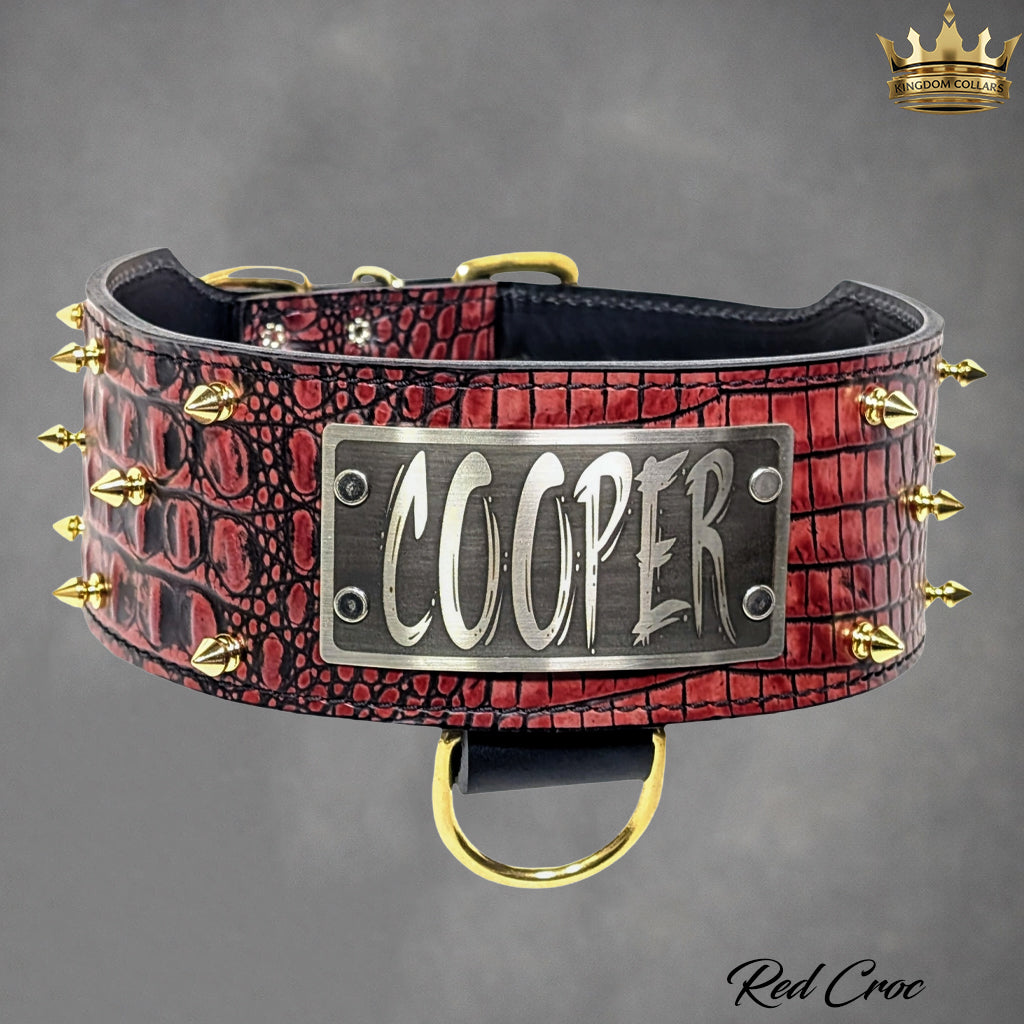 A red crocodile-embossed leather dog collar with gold-tone spikes and a central silver metal plate engraved with the name 'COOPER'.