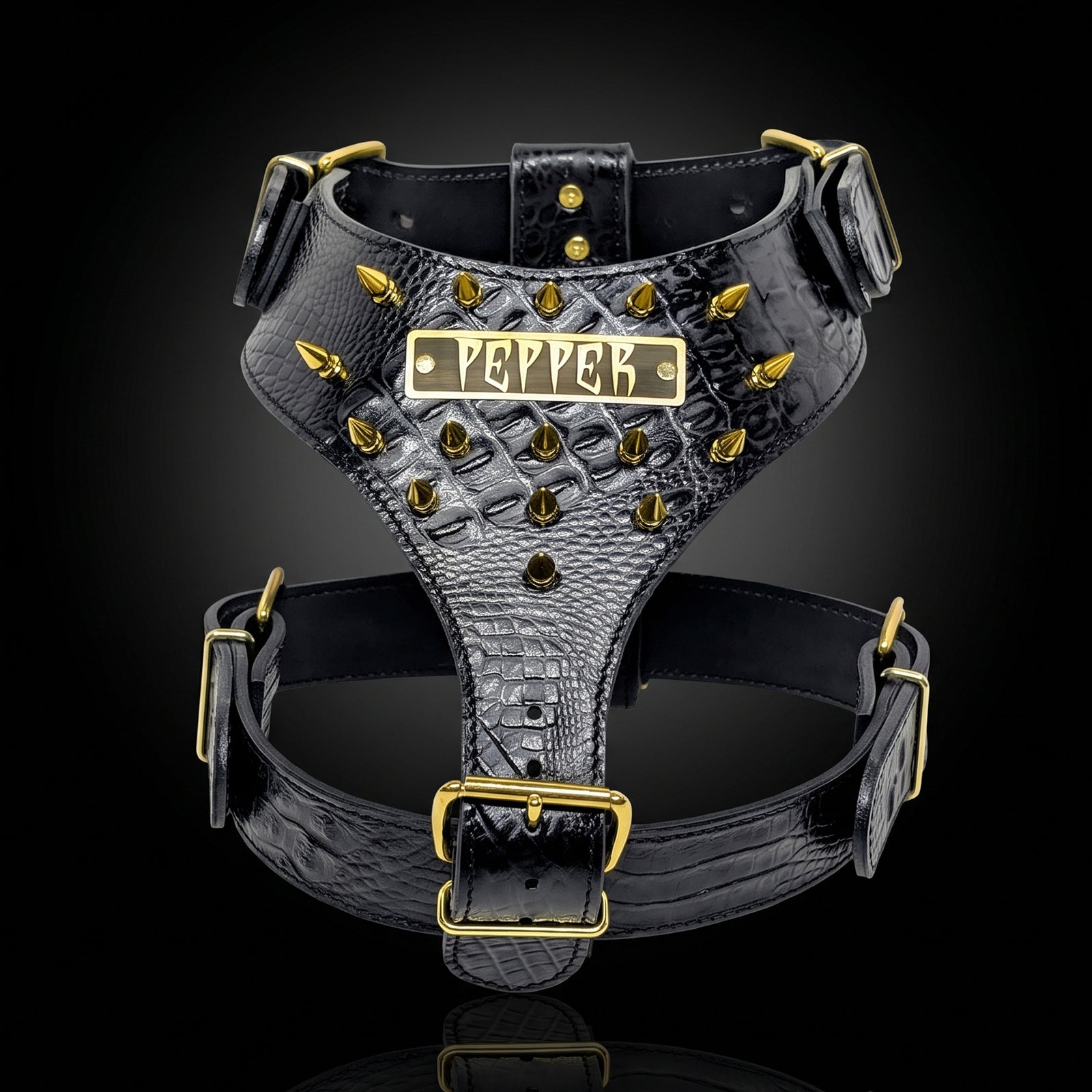 Black crocodile-embossed dog harness with gold hardware and a central nameplate reading 'PEPPER', shown on a black background.