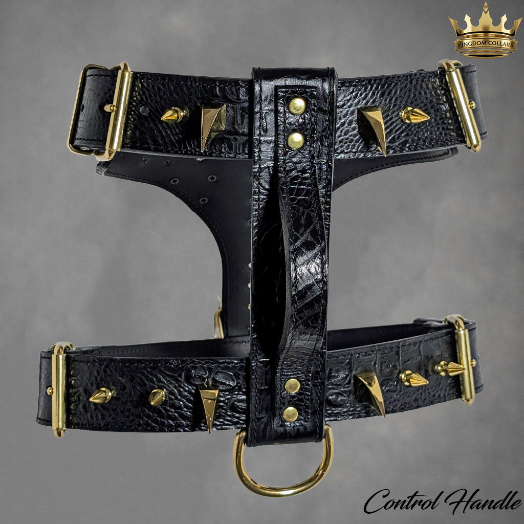 Black crocodile-embossed leather dog harness with gold-tone metal hardware, pyramid studs, and a central D-ring, shown on a gray background with a small crown logo and 'Control Handle' text.