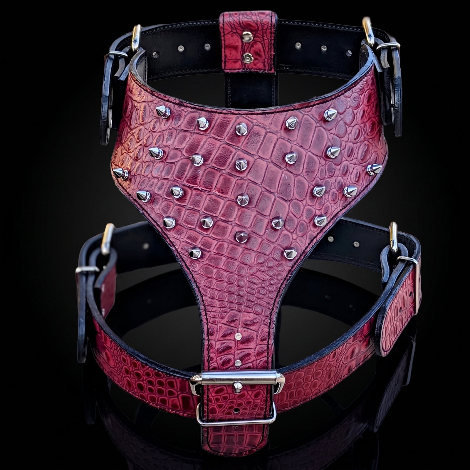 A red crocodile-embossed leather harness with silver metal studs and buckles, displayed against a black background.