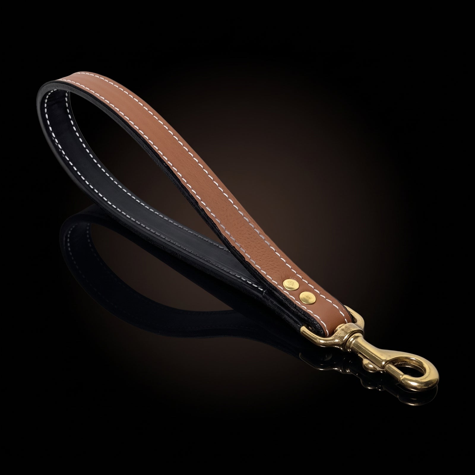 A brown leather dog leash with white contrast stitching, a black inner lining, and a gold-tone metal snap hook clasp, displayed on a reflective black background.