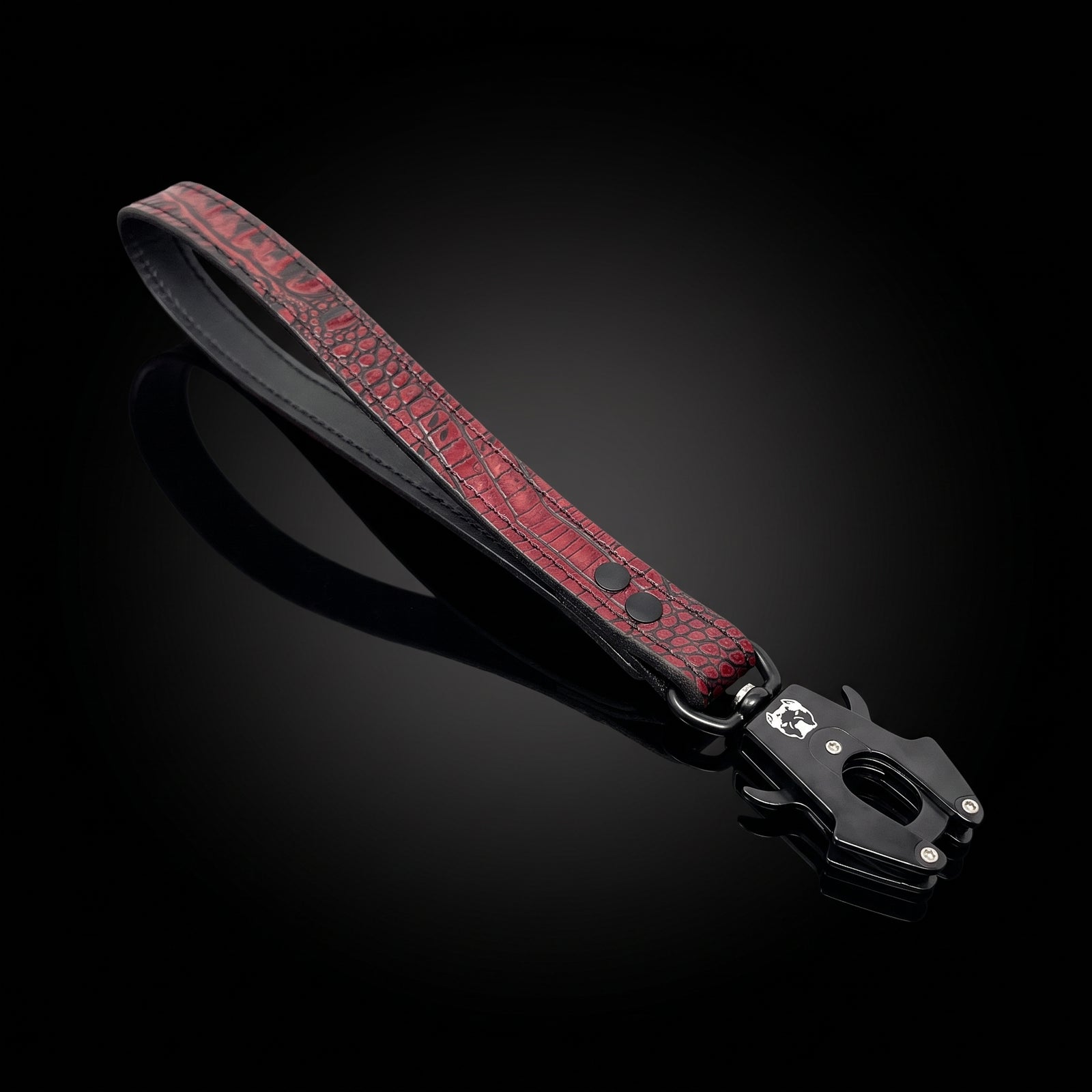 A red crocodile-embossed leather strap with black trim and a black metal clasp, displayed diagonally on a reflective black background.