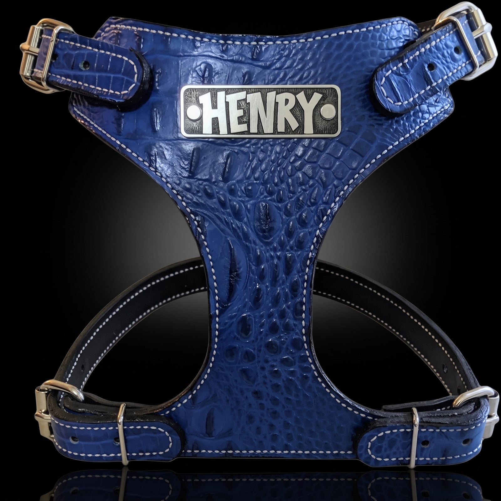 A royal blue crocodile-embossed dog harness with white contrast stitching and silver hardware, featuring a customizable metal nameplate on the chest that reads 'HENRY'.