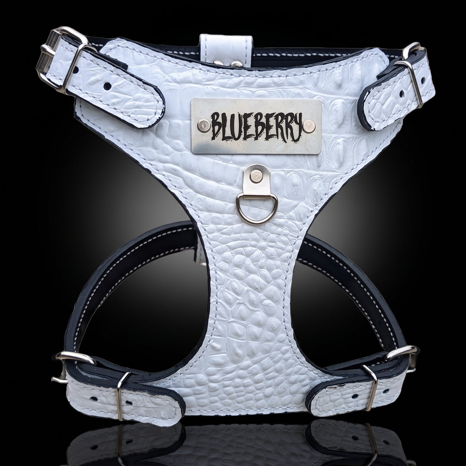 A white crocodile-embossed leather dog harness with dark gray trim and silver hardware, featuring a silver metal plate engraved with the brand name 'BLUEBERRY'.