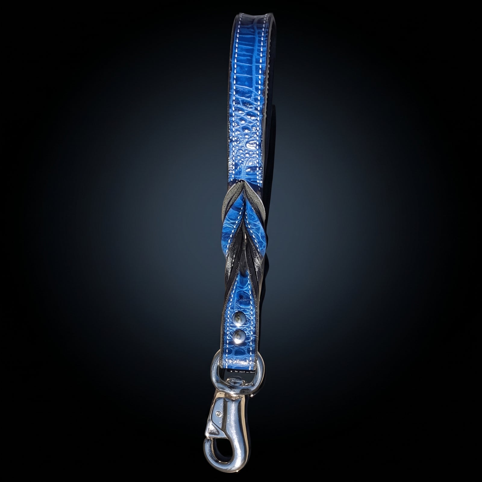 A blue alligator-textured leather dog leash with a braided center and a silver metal clasp, shown vertically against a dark gradient background.