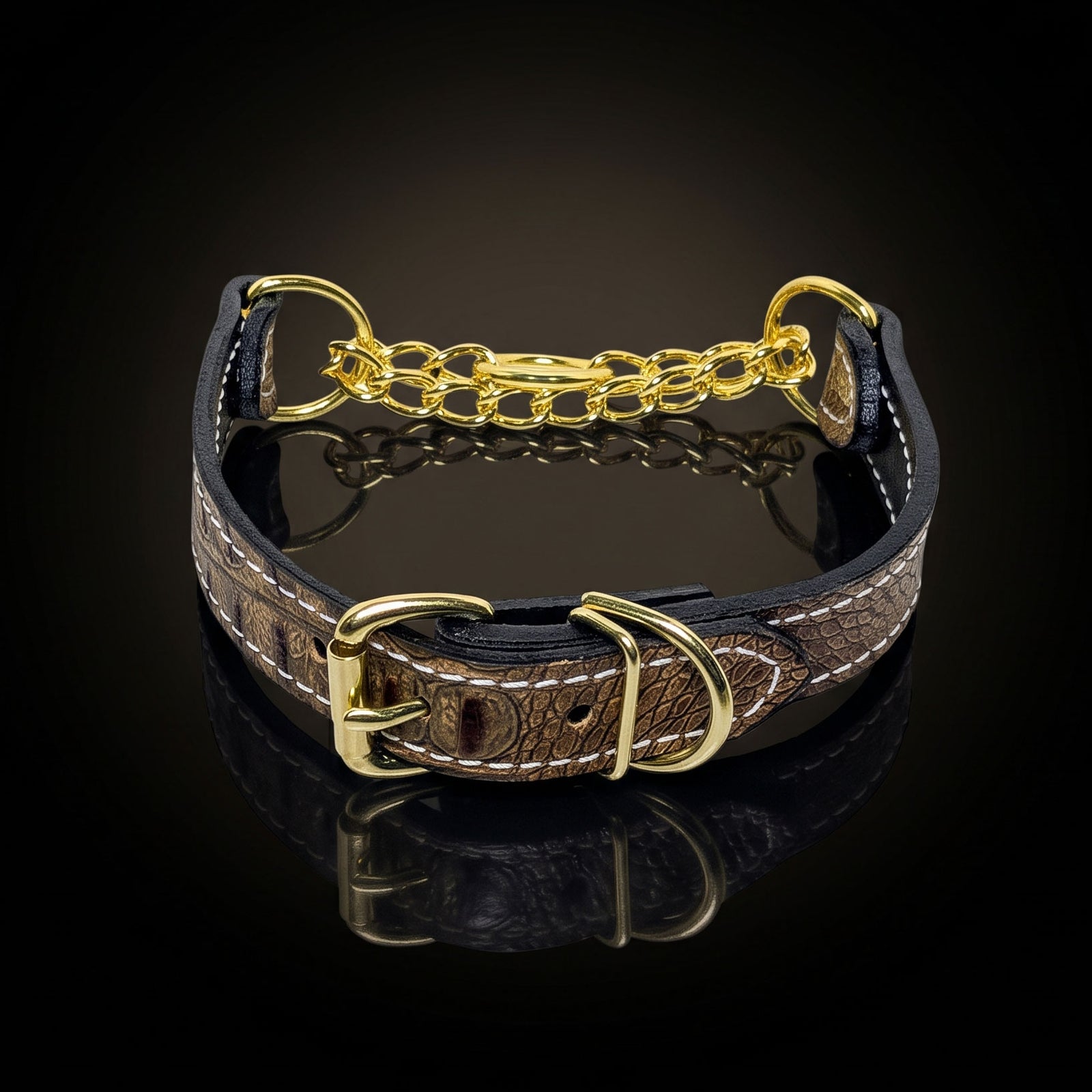 A brown crocodile-embossed leather dog collar with gold-tone hardware, including a chain link connector, D-rings, and buckle, displayed on a reflective black surface.