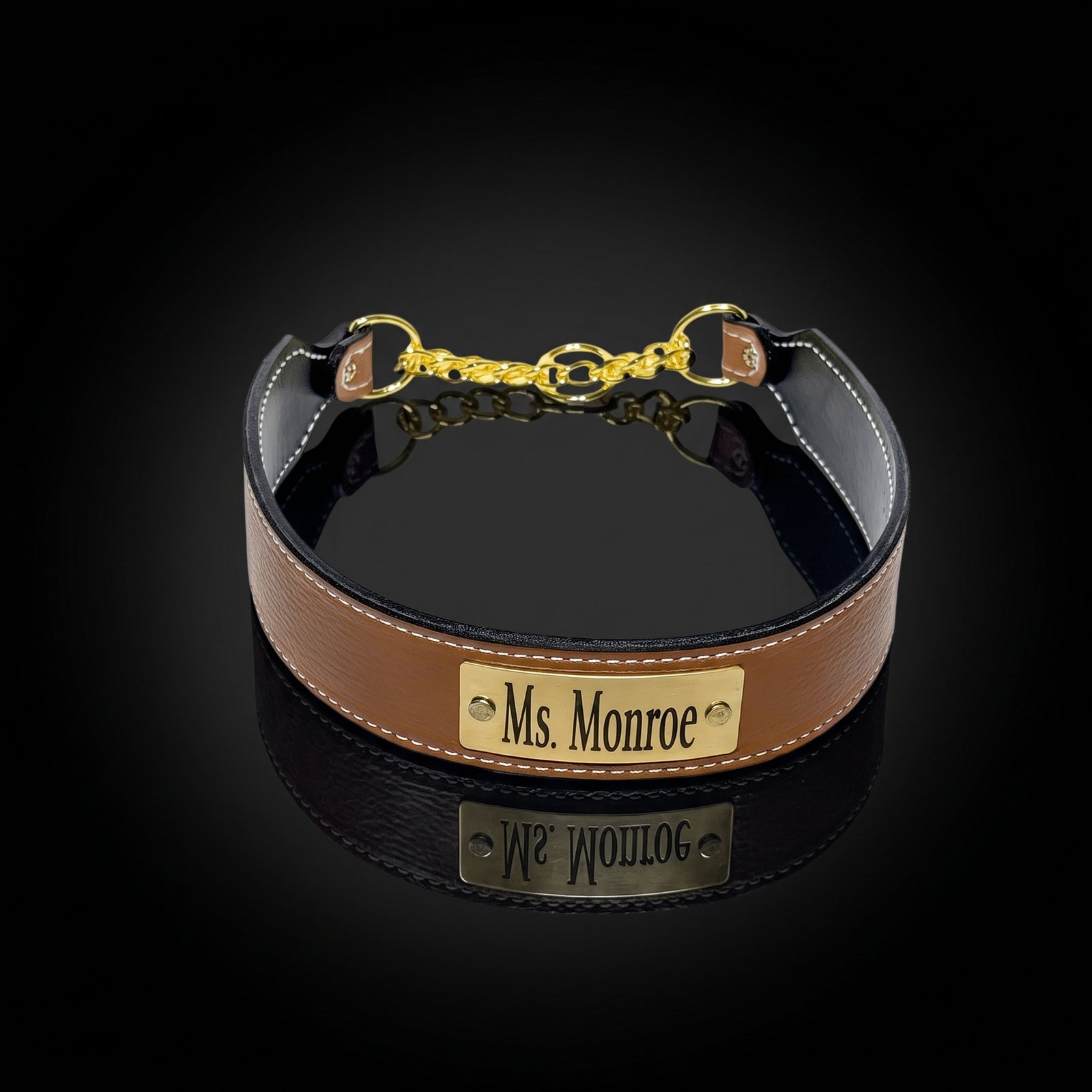 A brown leather collar with a black interior, white stitching, and gold-tone hardware, featuring a custom brass plate engraved with 'Ms. Monroe'.