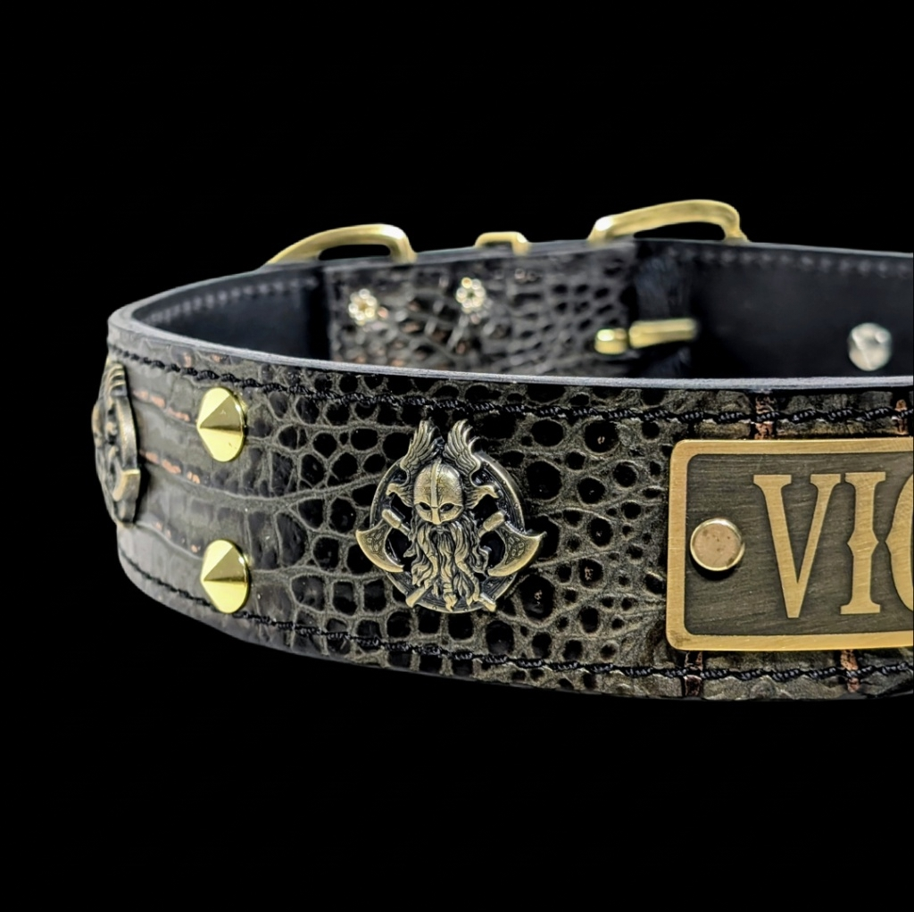 Black crocodile-embossed leather collar with gold-tone hardware, featuring a central skull-and-wings emblem and a rectangular nameplate engraved with 'VIC'.