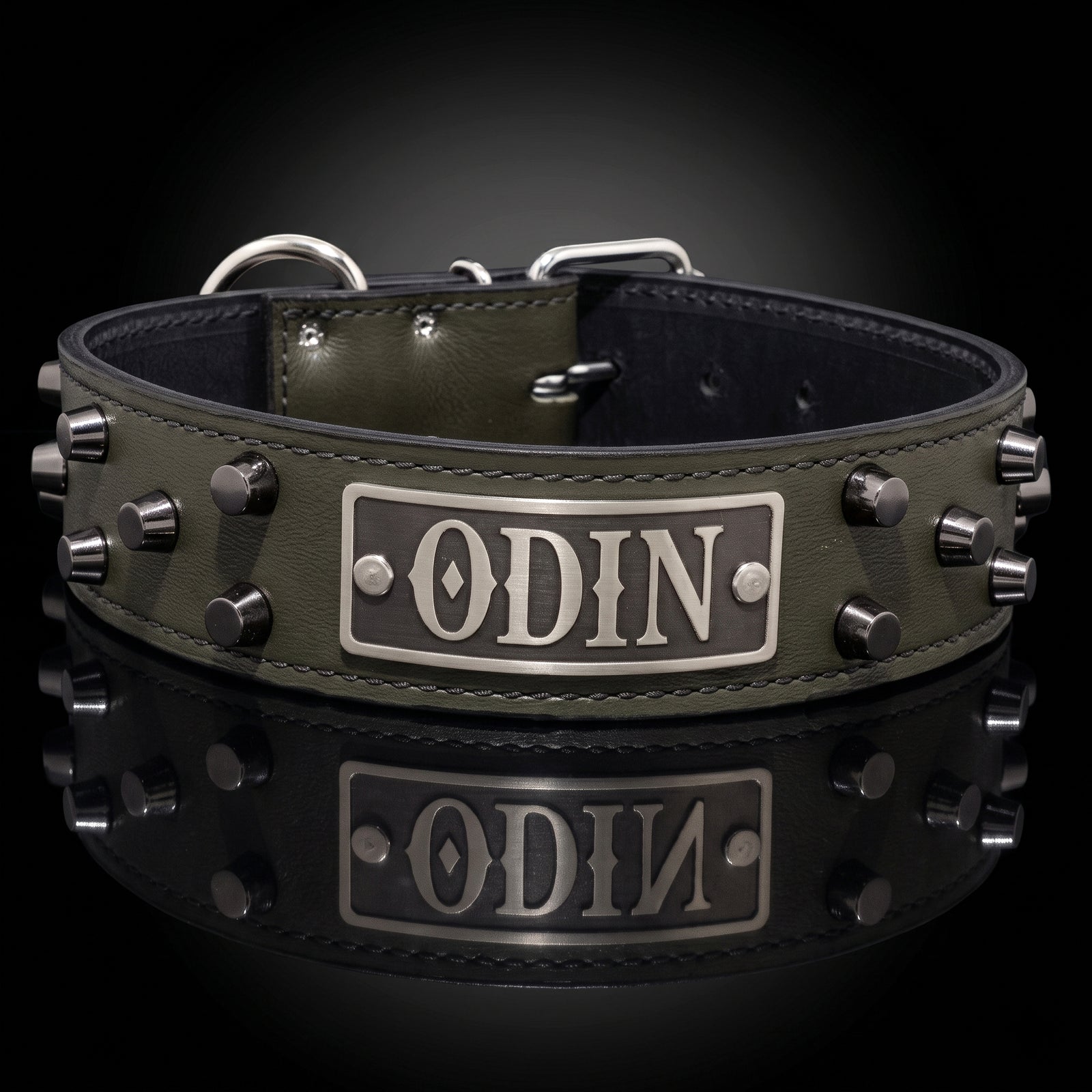 An olive green leather dog collar with silver metal studs and a central rectangular plate engraved with the name 'ODIN'. The collar is displayed on a reflective black surface against a dark gradient background.
