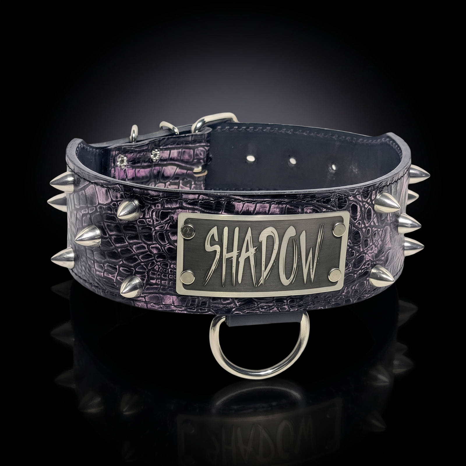 A dark purple and black crocodile-embossed leather dog collar with silver-tone spikes and a central metal plate engraved with the name 'SHADOW'.
