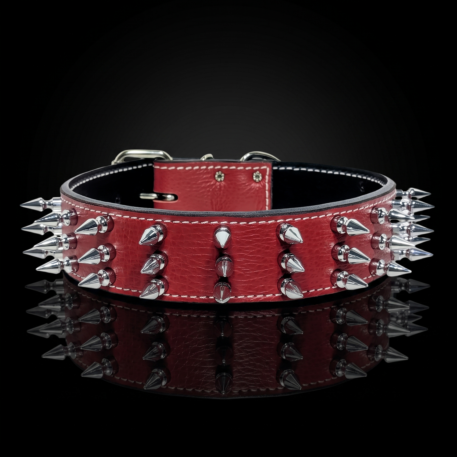 A red leather dog collar with silver metal spikes and white stitching, displayed on a reflective black surface.