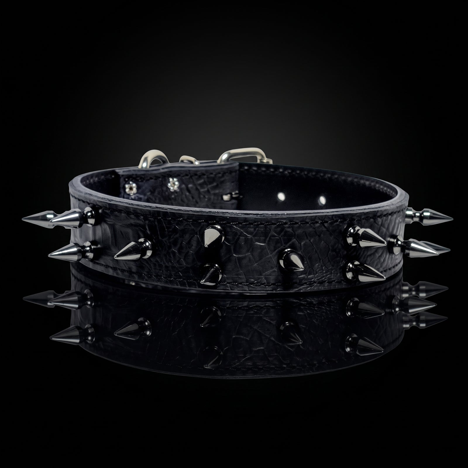 A black crocodile-embossed leather dog collar with sharp silver metal spikes and studs, displayed on a reflective black surface against a dark background.