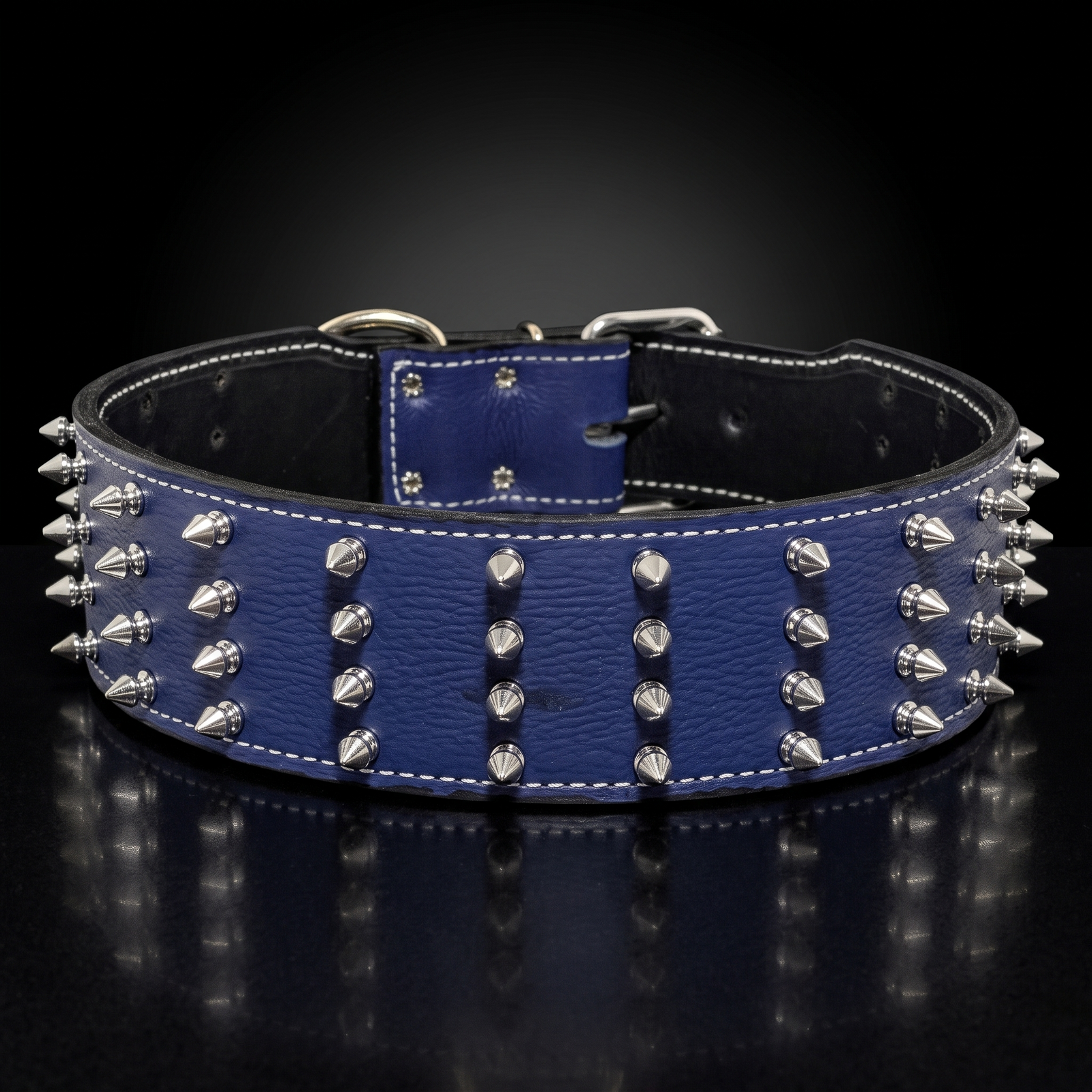 A blue leather collar with silver metal spikes and white stitching, displayed on a reflective black surface against a dark gradient background.