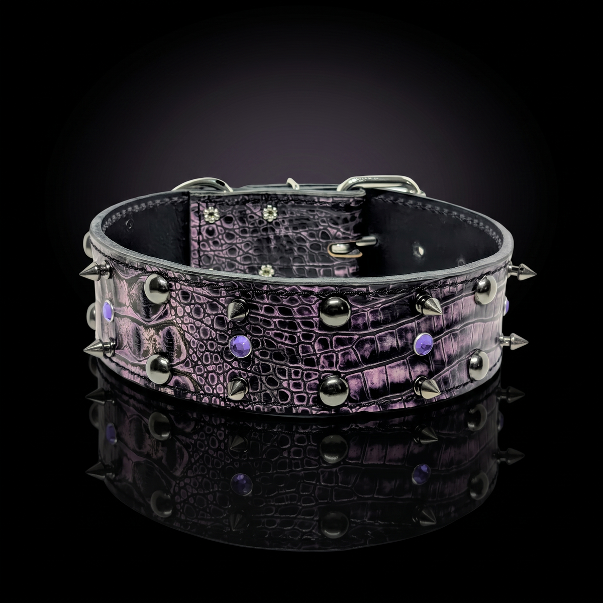 A wide black crocodile-embossed leather collar with silver-toned spikes and studs, accented with small purple gemstones, displayed on a reflective black surface.