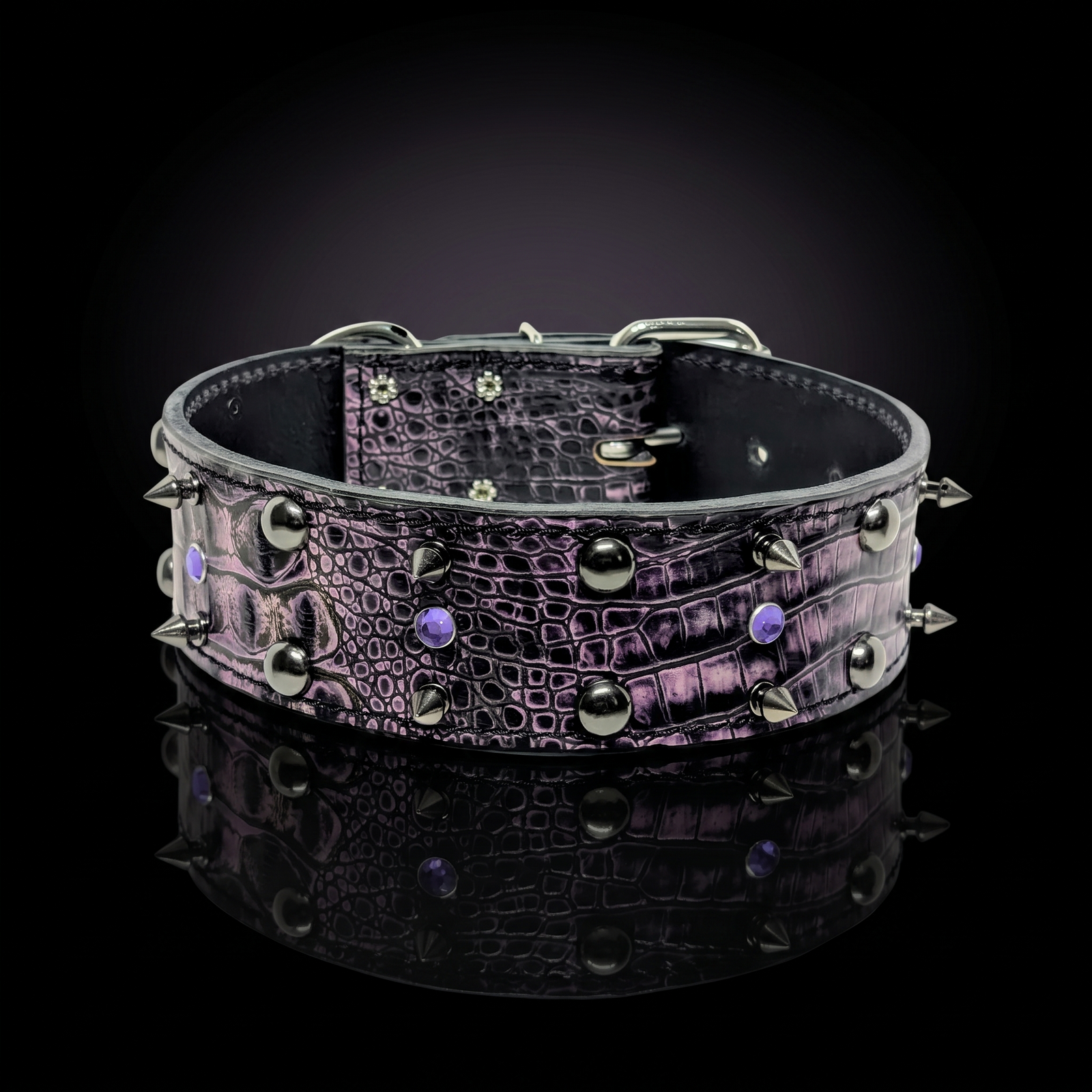 A wide black crocodile-embossed leather collar with silver-toned spikes and studs, accented with small purple gemstones, displayed on a reflective black surface.