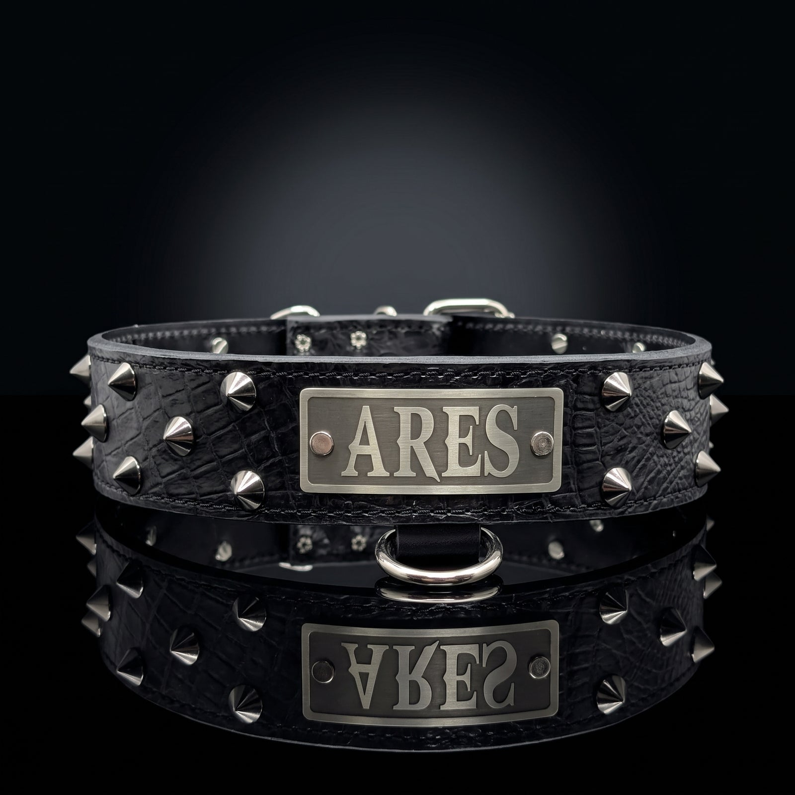A black crocodile-embossed leather collar with silver-tone spikes and a central rectangular metal plate engraved with the name 'ARES', shown on a dark reflective surface.