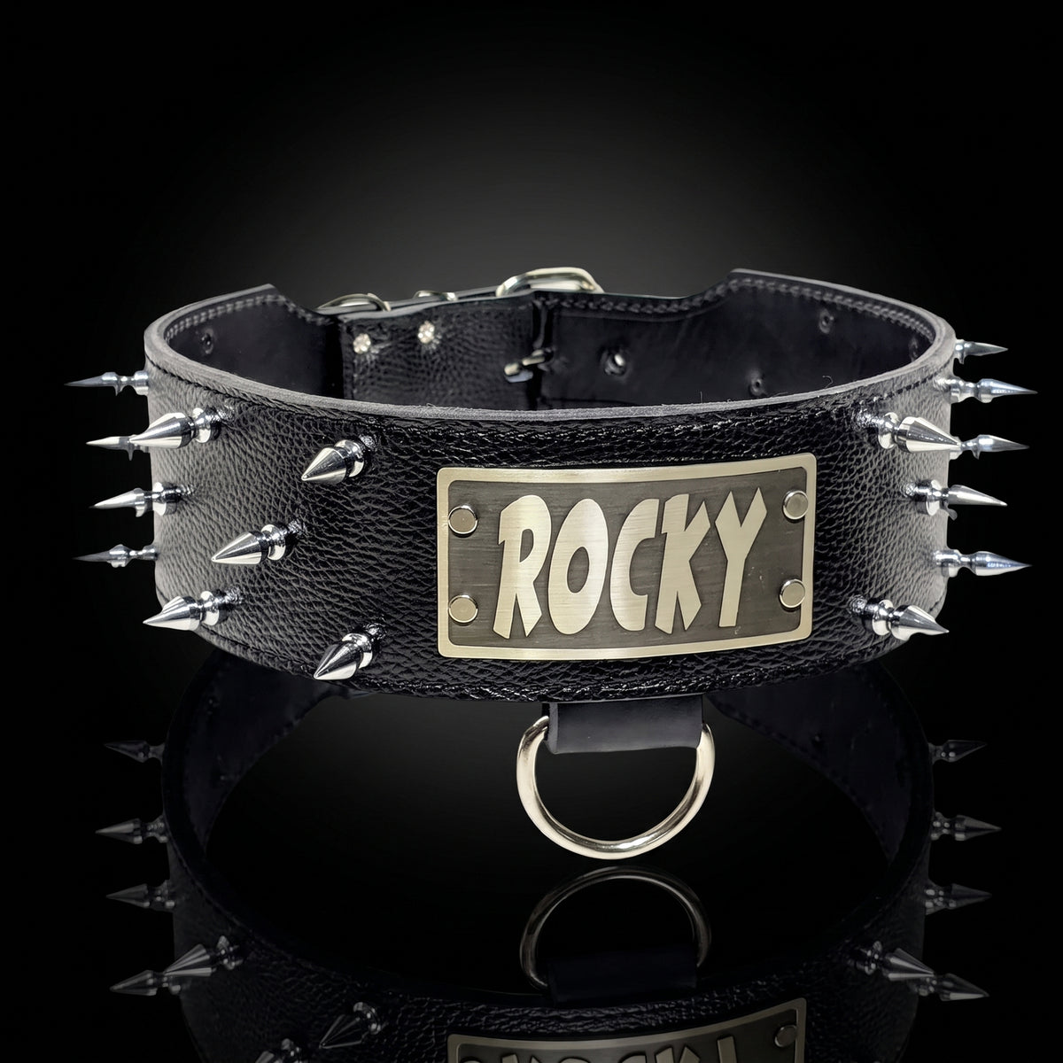 A black textured leather spiked collar with a rectangular brass plate engraved with the name 'ROCKY' in stylized letters, displayed on a reflective black surface against a dark background.