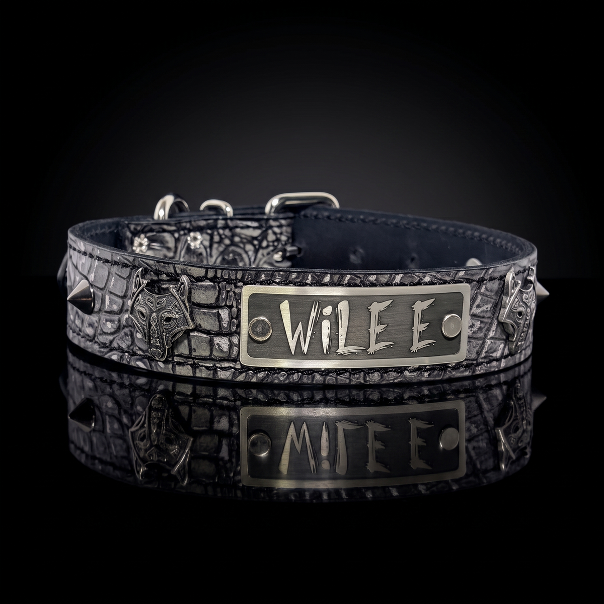 A dark textured dog collar with a central silver-tone metal plate engraved with 'WILE E', displayed on a reflective black surface against a black background.