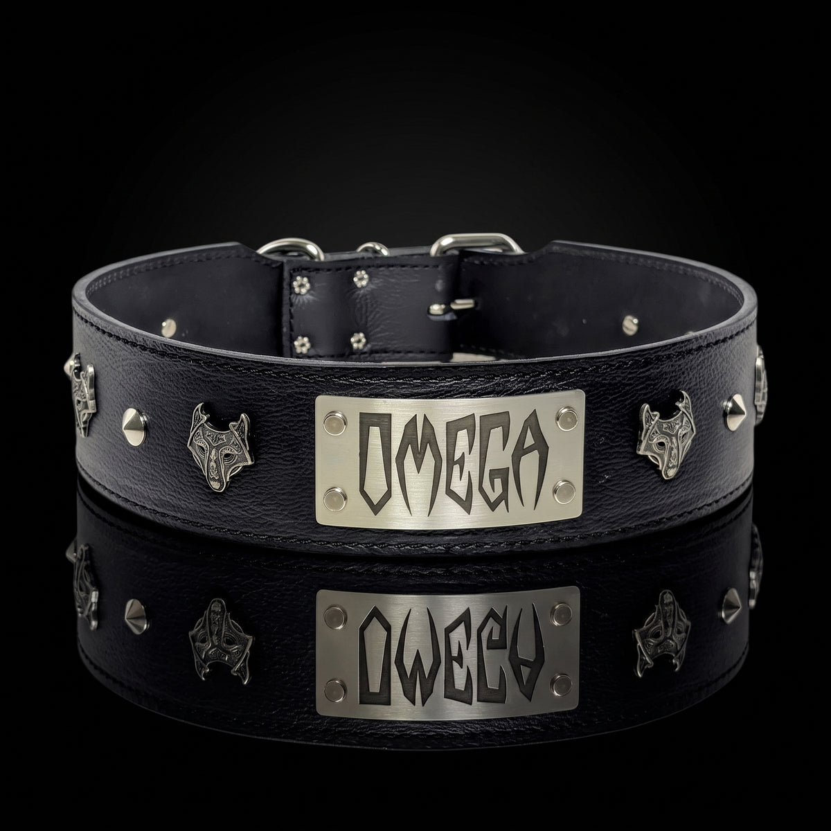 A black leather collar with silver metal studs, wolf head emblems, and a central rectangular silver plate engraved with the word 'OMEGA', shown on a black background with a reflection below.