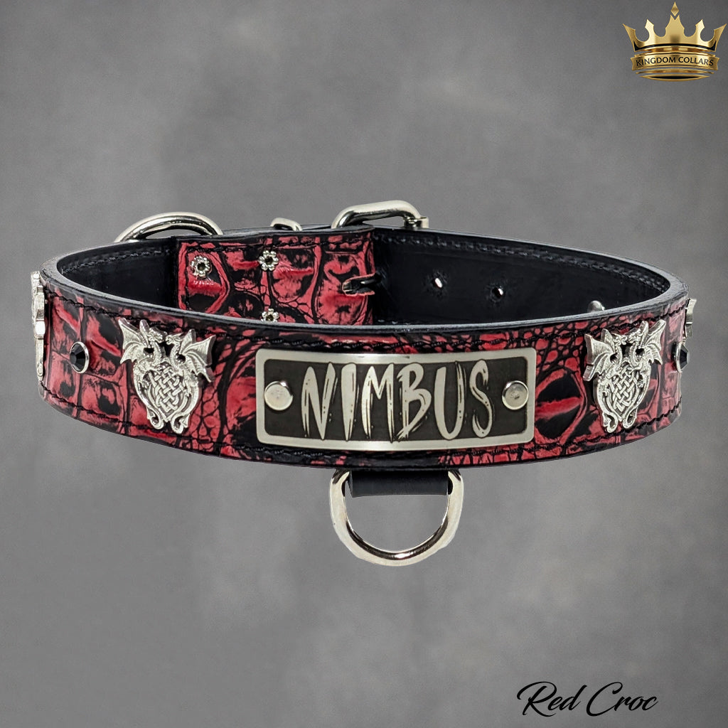 A red crocodile-patterned leather dog collar with silver hardware, featuring a central silver plate engraved with 'NIMBUS', decorative silver wolf head studs, and a black buckle closure, shown on a gray background.