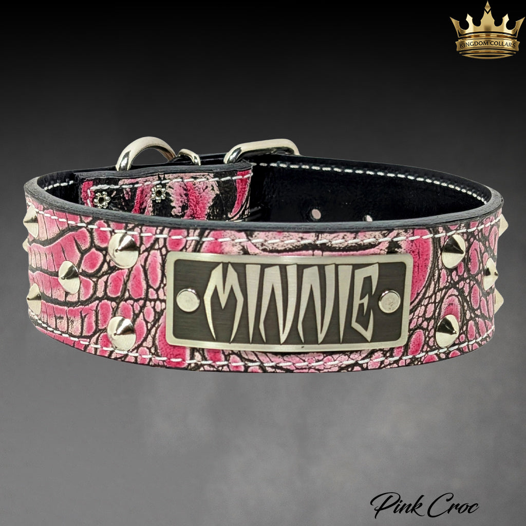 A pink and black crocodile-embossed leather dog collar with silver-tone metal studs and a central metal plate engraved with the name 'MINNIE'.