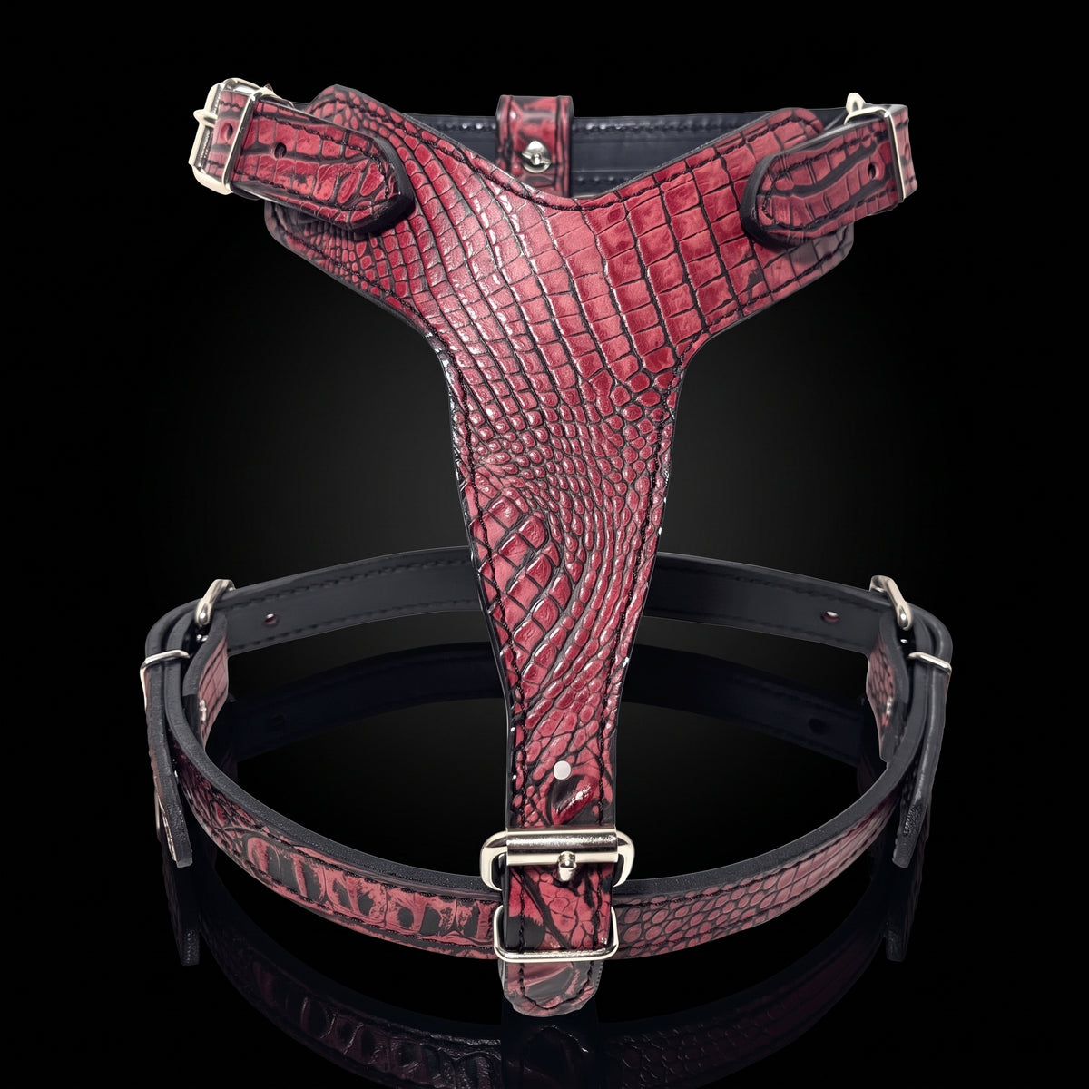 A red crocodile-embossed leather dog harness with silver metal hardware, displayed on a reflective black background.