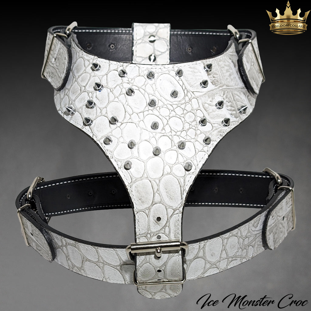 A white crocodile-embossed leather harness with silver studs and black adjustable straps, displayed against a dark gray gradient background. A gold crown logo for 'Ice Monster Croc' is visible in the top right corner.