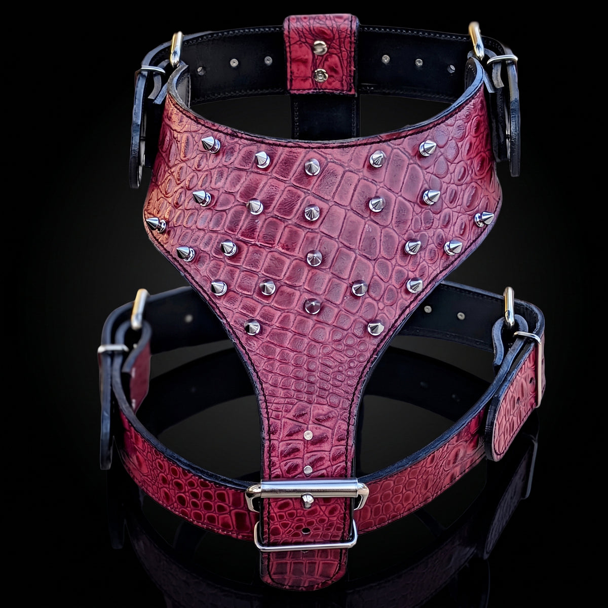 A red crocodile-embossed leather harness with silver metal studs and buckles, displayed against a black background.