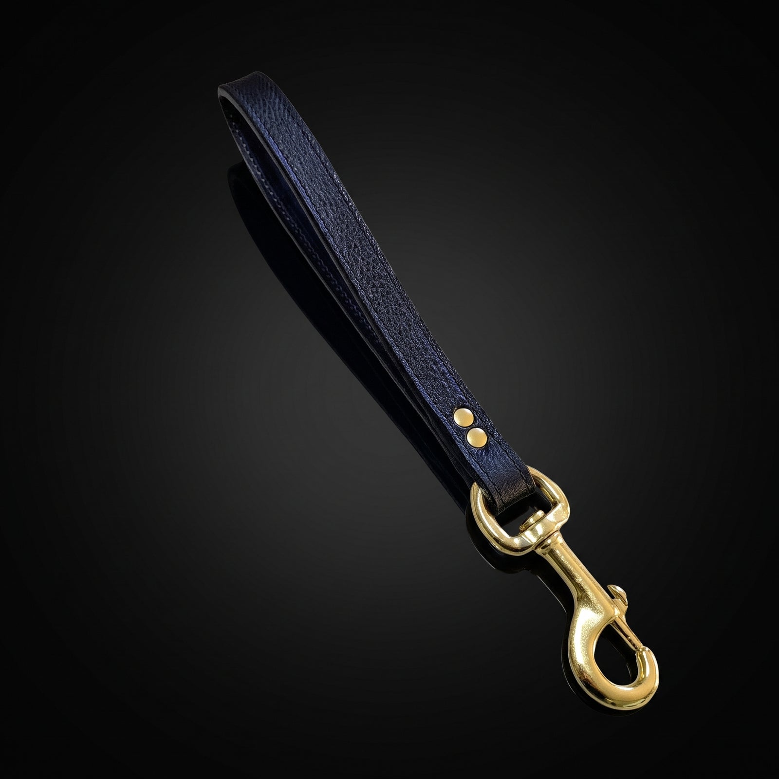 A black textured leather strap with a polished gold-tone metal swivel snap hook, displayed diagonally on a dark reflective background.