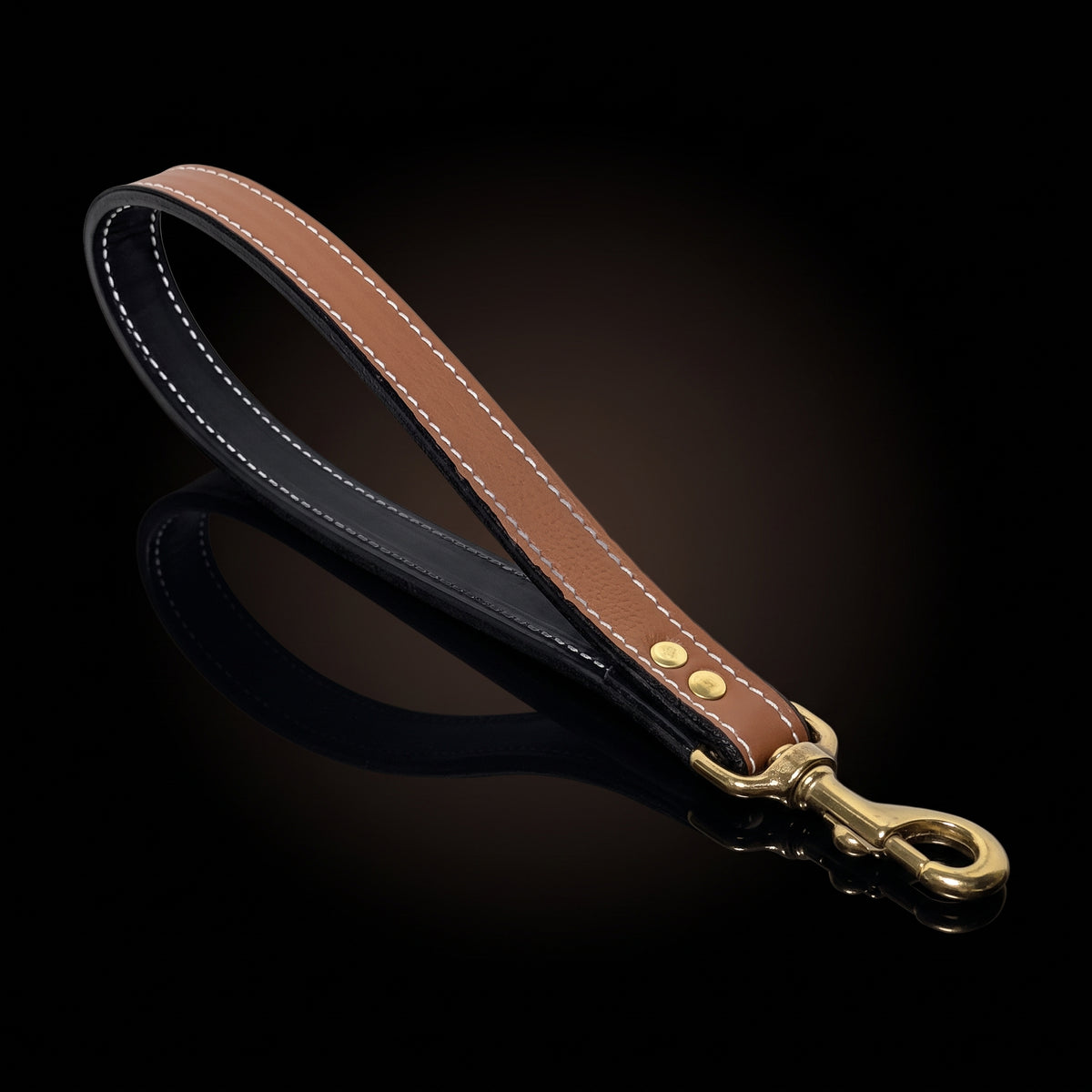 A brown leather dog leash with white contrast stitching, a black inner lining, and a gold-tone metal snap hook clasp, displayed on a reflective black background.