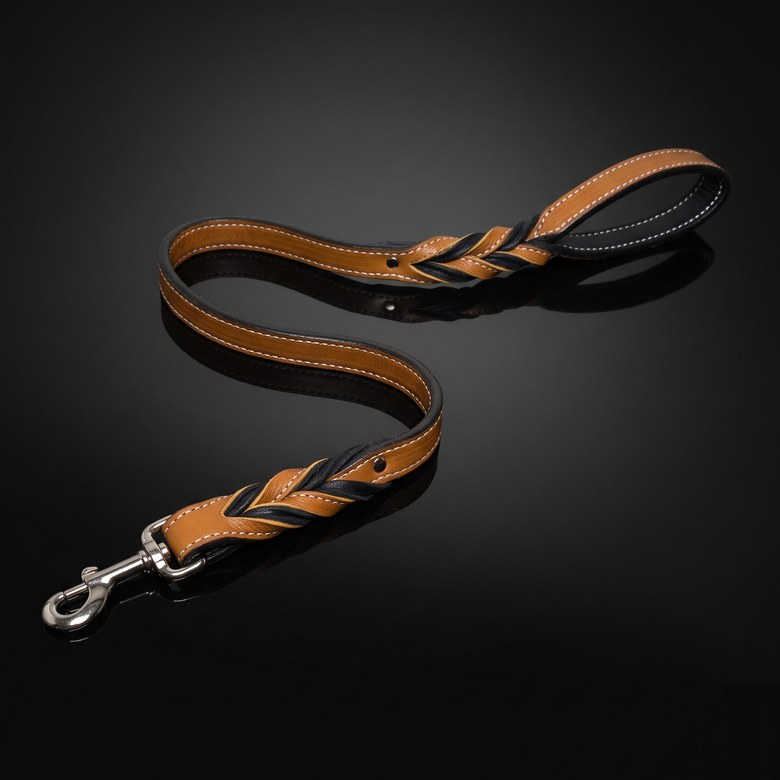 A premium handcrafted dog leash featuring a twisted brown and black leather design with white stitching and a heavy-duty silver metal snap hook, displayed on a dark reflective background.