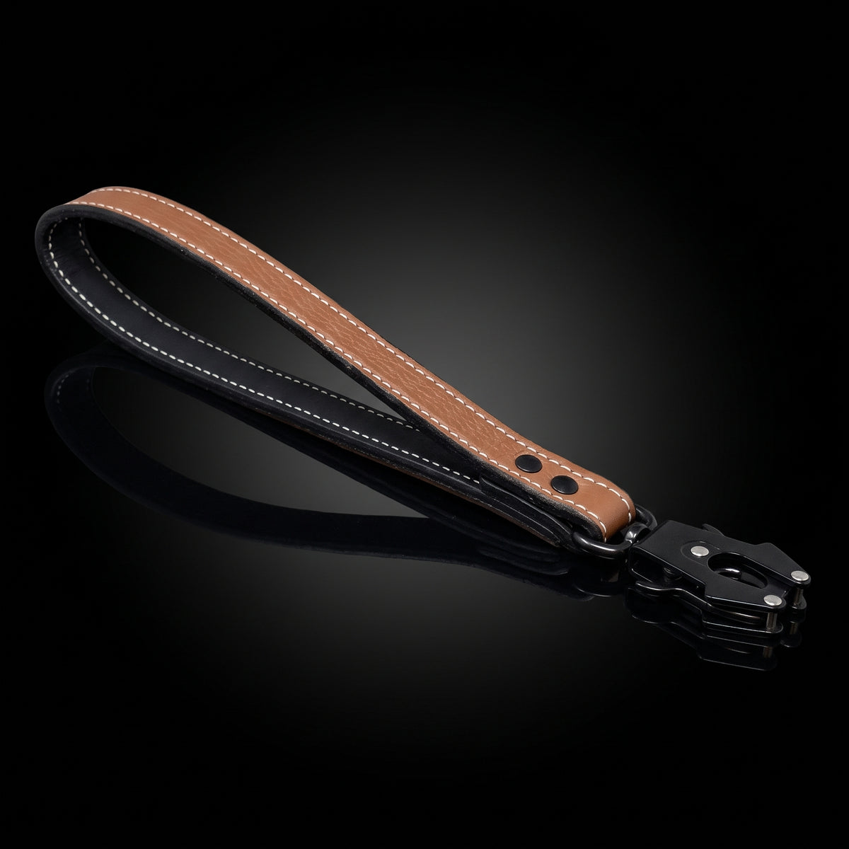 A brown leather wrist strap with white contrast stitching and a black metal clasp, displayed on a reflective black background.