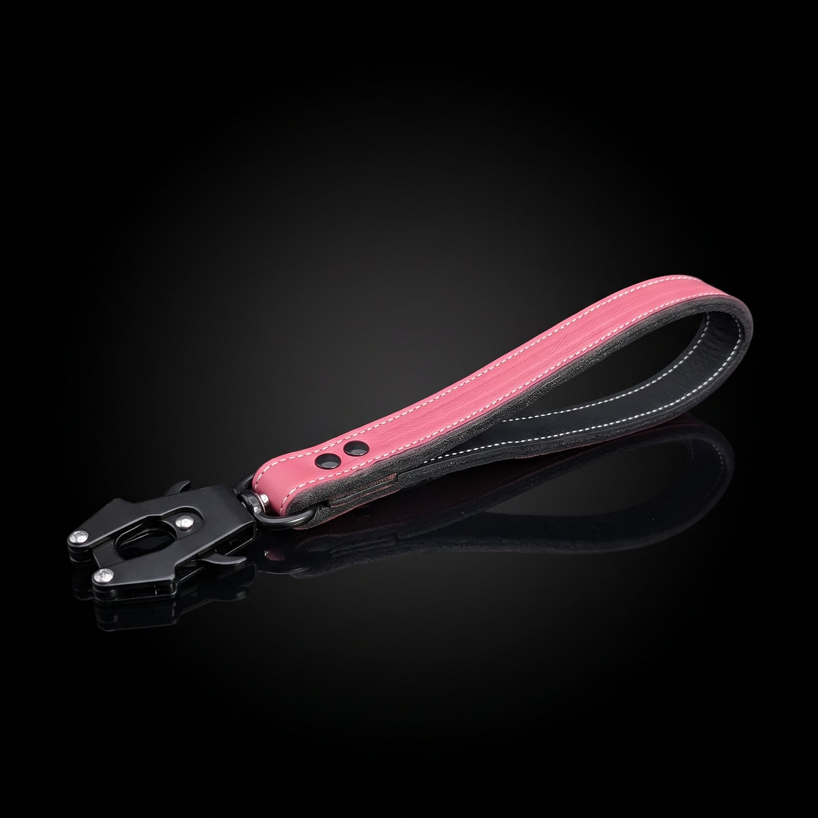 A pink leather strap with a black metal lock mechanism, displayed on a reflective black surface against a dark gradient background.
