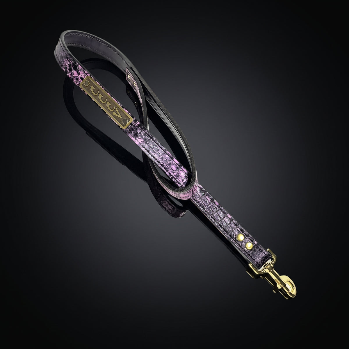 A purple and black crocodile-embossed leather strap with gold-tone hardware, shown on a reflective black background.
