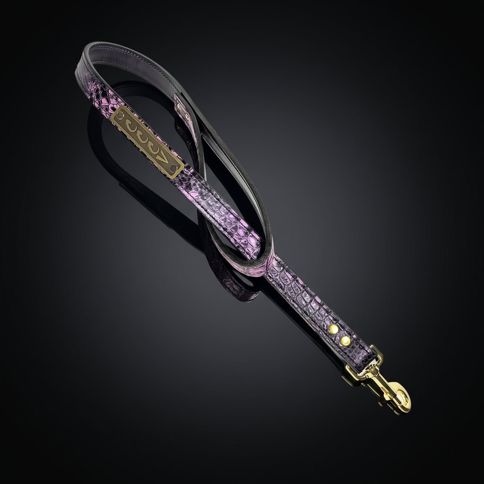 A purple and black crocodile-embossed leather strap with gold-tone hardware, shown on a reflective black background.