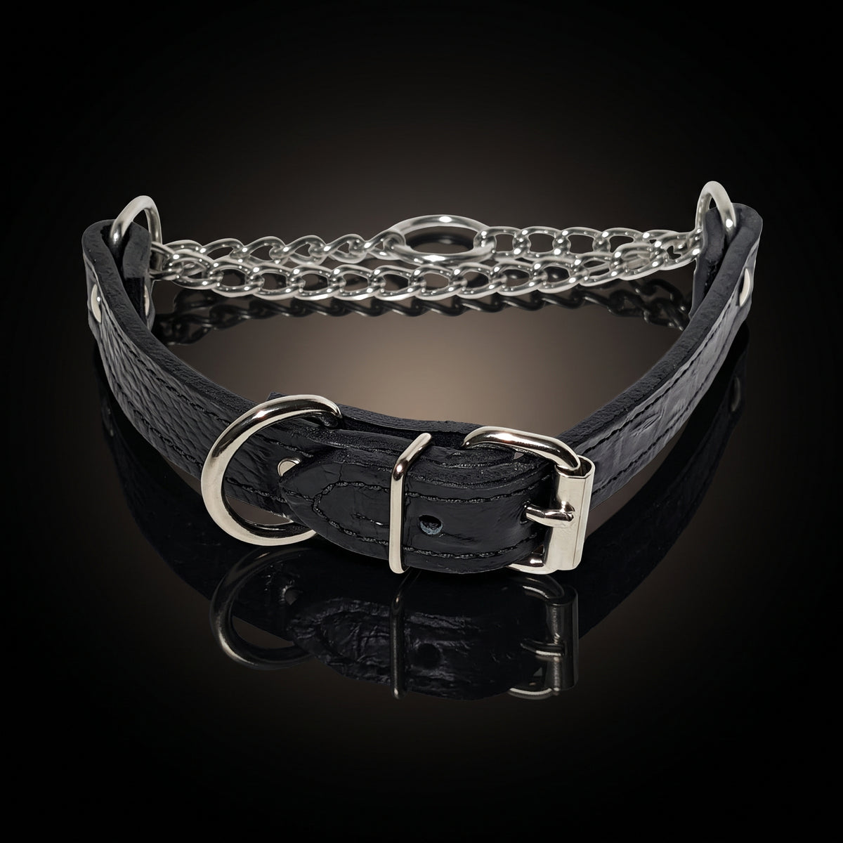 A black crocodile-embossed leather collar with silver-tone metal hardware, including a chain link section, a large D-ring, and a buckle, displayed on a reflective black surface.