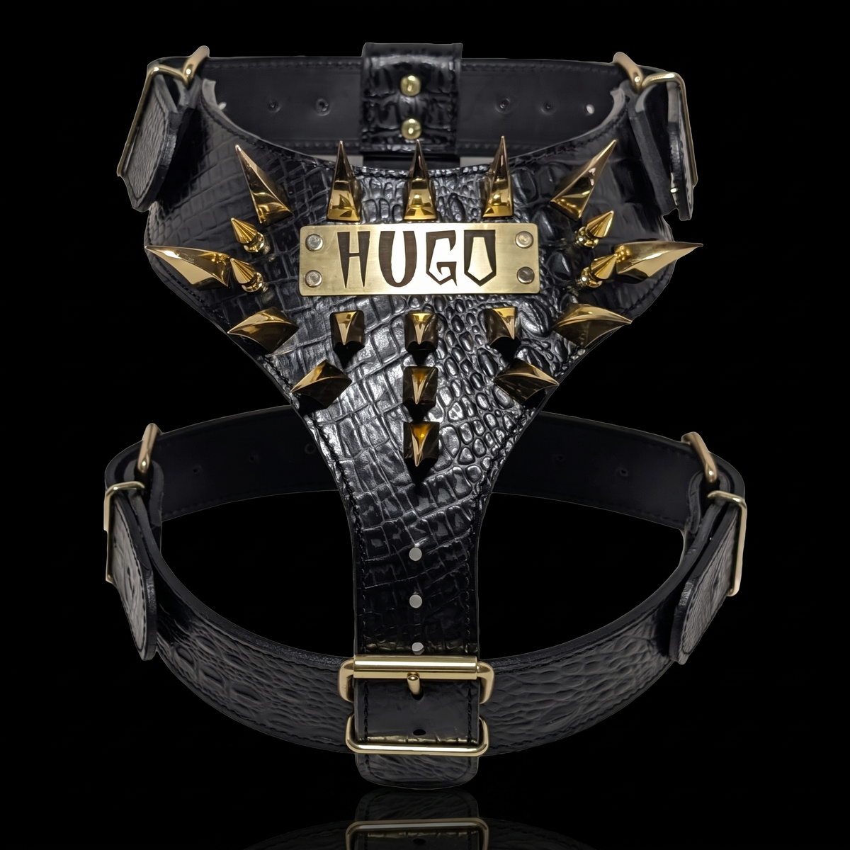 Black crocodile-embossed leather dog harness with gold-tone spikes and a central metal plate engraved with 'HUGO', shown on a black background.