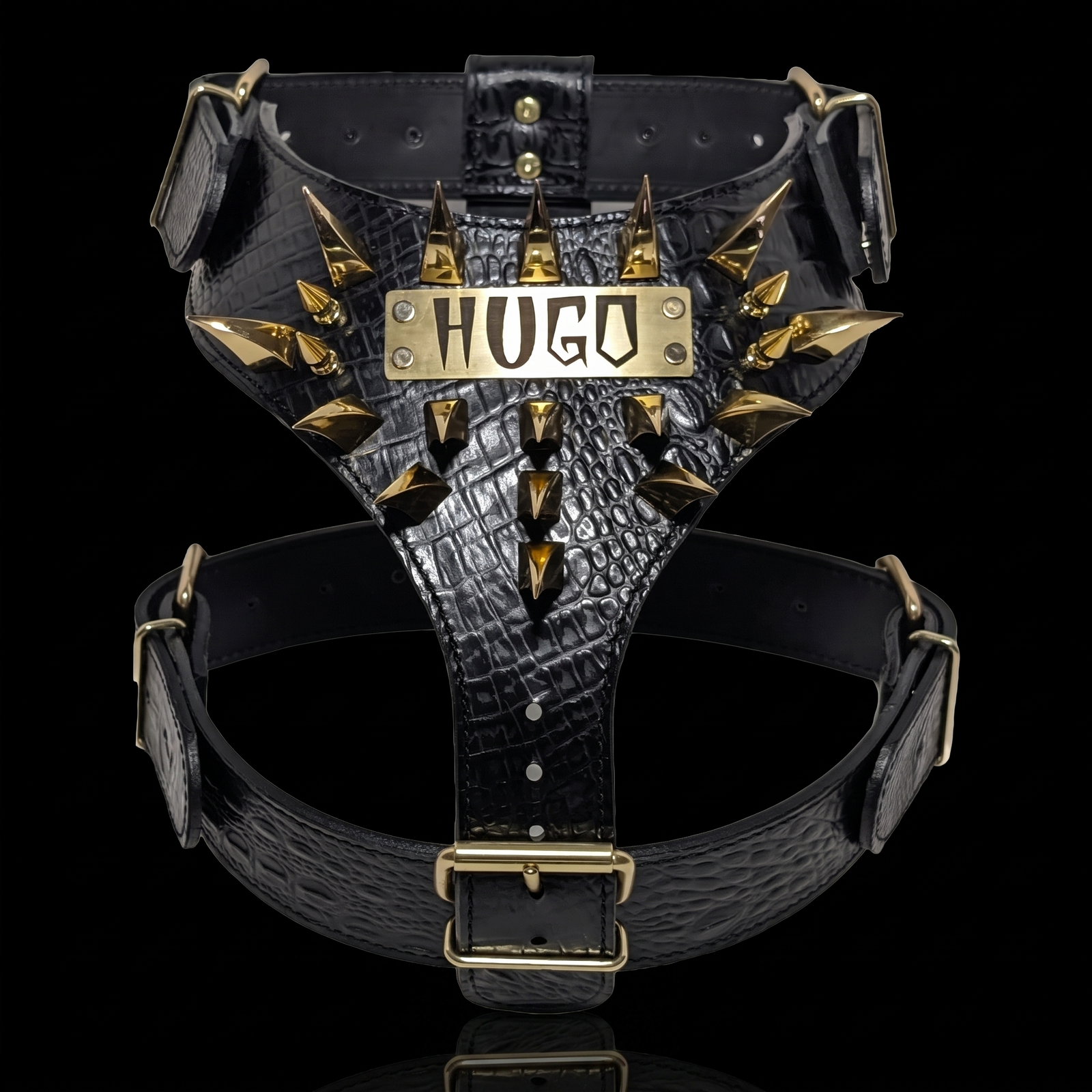 Black crocodile-embossed leather dog harness with gold-tone spikes and a central metal plate engraved with 'HUGO', shown on a black background.