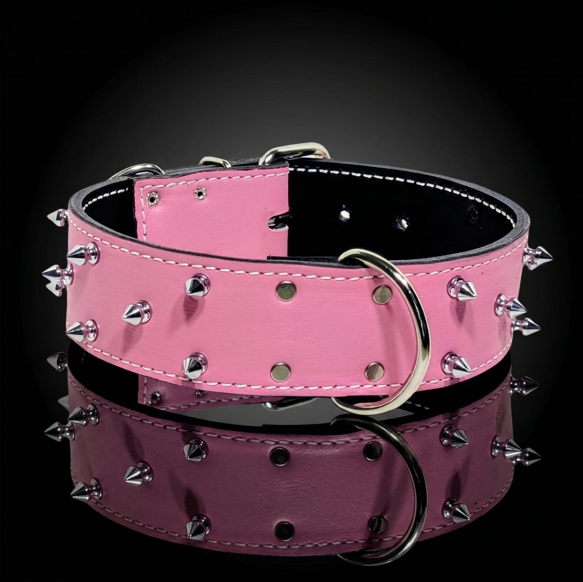 A pink leather dog collar with silver metal spikes and a large silver D-ring, displayed on a reflective black surface.