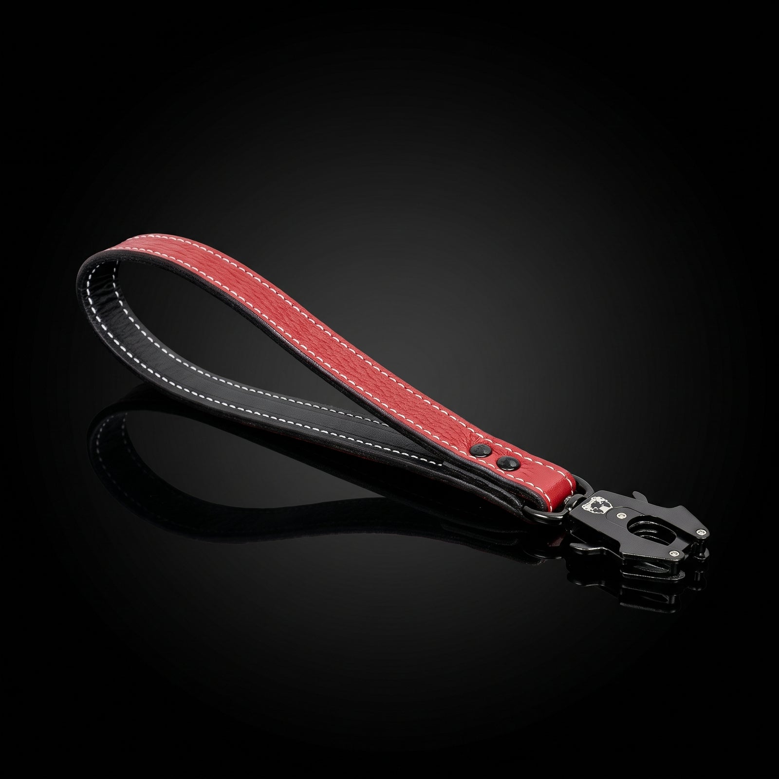 A red leather strap accessory with white contrast stitching and a black metal clasp, displayed on a reflective black background.