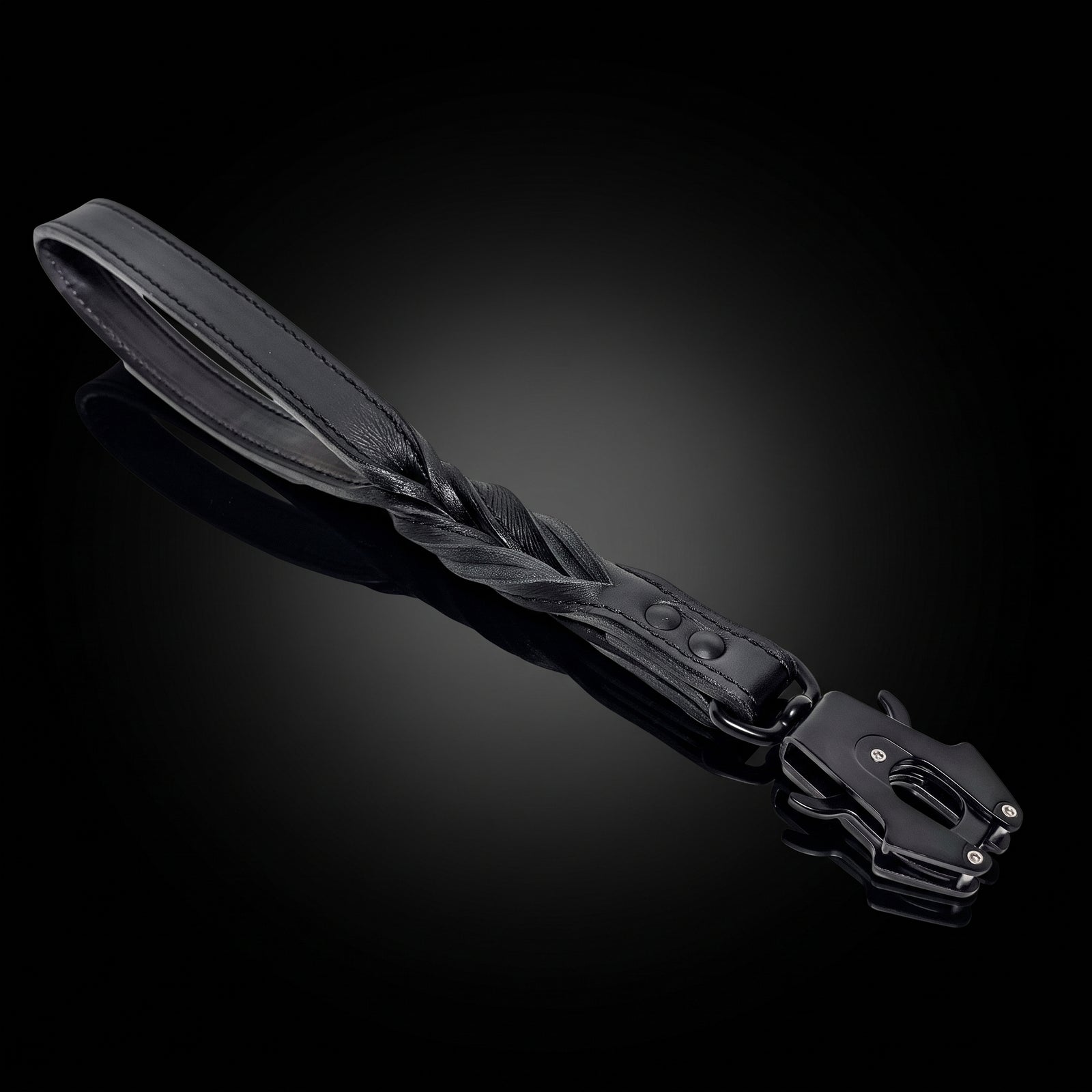 A black leather strap accessory with a braided center section and a black metal buckle, photographed on a dark reflective studio background.