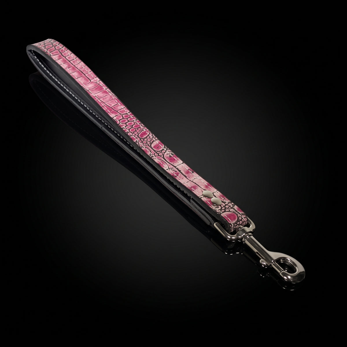 A pink crocodile-embossed leather strap with silver-tone hardware, shown diagonally on a reflective black background.